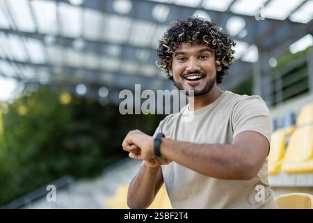 L'homme utilise un bracelet de fitness de montre intelligente pendant l'entraînement. Athlète est satisfait des résultats de son entraînement, sourit et regarde la caméra. Banque D'Images