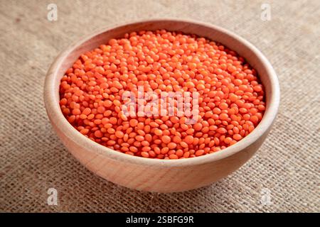 Un bol en bois avec des grains de lentilles rouges sur une toile de jute. Vue de dessus des lentilles orange séchées à l'intérieur du bol. Banque D'Images