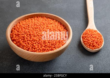 Grains de lentilles rouges dans un bol en bois et cuillère sur fond gris. Vue de dessus des lentilles orange séchées à l'intérieur du bol. Banque D'Images