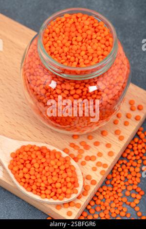 Sur une planche à découper, il y a une cuillère remplie de lentilles orange et un bocal en verre rempli de lentilles rouges Banque D'Images