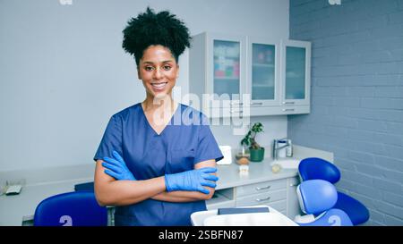 Dentiste professionnel souriant dans le cabinet dentaire moderne, portant des gommages et des gants Banque D'Images
