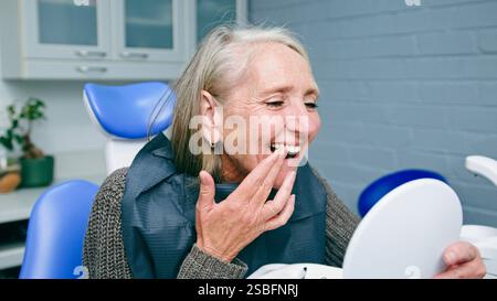 Femme âgée souriante admirant ses dents lors d'une visite chez le dentiste Banque D'Images
