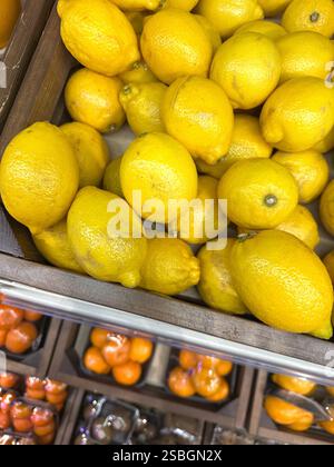 Citrons jaunes colorés CITRUS LIMON et quelques mandarines floues, sur le comptoir d'un magasin de fruits et légumes dans une boîte en bois, gros plan. Banque D'Images
