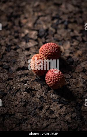 Trois litchis reposant sur une surface sombre fissurée, une étude en contraste Banque D'Images