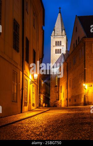 Vue en soirée sur le clocher de la basilique Saint-Georges depuis la rue Jirska, illuminée par des lampadaires et mettant en valeur l'architecture historique de Prague. Banque D'Images