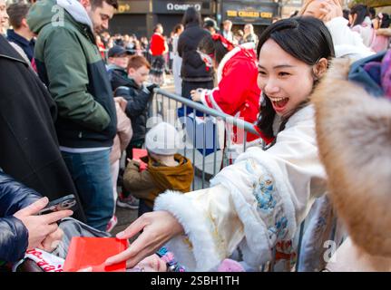 Souriante jeune femme asiatique distribue des enveloppes rouges ou hongbau à la parade du nouvel an chinois CNY 2025 à Newcastle upon tyne, royaume-uni - année du serpent Banque D'Images