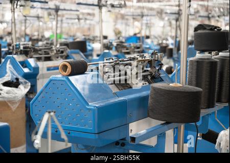 Vue de machines automatisées de fabrication de textiles dans une usine, avec des bobines de fil blanc prêtes pour le traitement. Banque D'Images