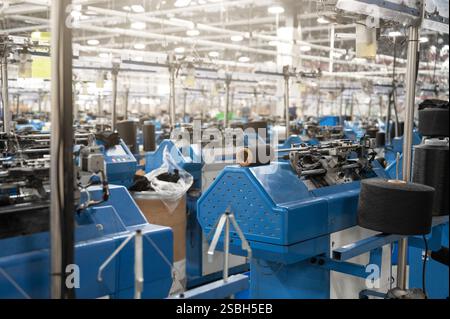 Vue de machines automatisées de fabrication de textiles dans une usine, avec des bobines de fil blanc prêtes pour le traitement. Banque D'Images