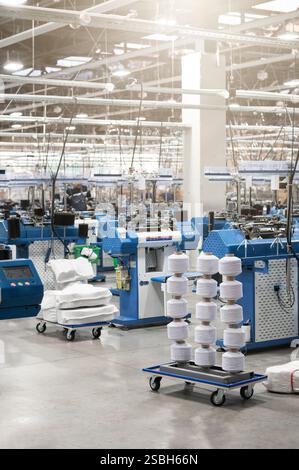 Vue de machines automatisées de fabrication de textiles dans une usine, avec des bobines de fil blanc prêtes pour le traitement. Banque D'Images