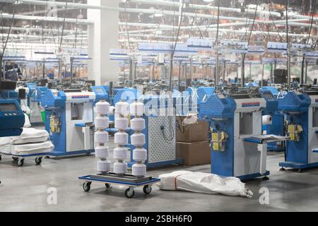 Vue de machines automatisées de fabrication de textiles dans une usine, avec des bobines de fil blanc prêtes pour le traitement. Banque D'Images