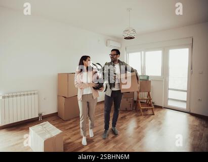 Couple heureux transportant des boîtes en carton et des plantes dans un appartement vide. Déballage des boîtes et déménagement dans une nouvelle maison ensemble Banque D'Images