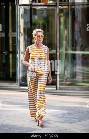 Belle femme mature avec les cheveux courts dans des vêtements élégants costume rayé, Accessoires à la mode et chaussures élégantes Walking City Streets le jour de l'été. Banque D'Images