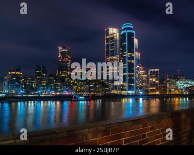 Londres, Royaume-Uni - 27 octobre 2024 : un paysage urbain animé de Londres la nuit avec des gratte-ciel illuminés reflétant sur une rivière calme de la Tamise. Banque D'Images