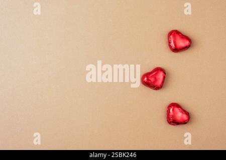 Bonbons à coeurs rouges sur une surface beige, symbolisant l'amour et la romance dans une composition minimaliste et élégante. Concept de la Saint-Valentin. Vue de dessus, plat Banque D'Images