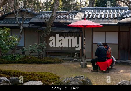 Couple japonais prenant une pause sur un banc sous un parapluie rouge est un espace de jardin calme au temple bouddhiste zen Kodaiji à Kyoto, au Japon. Banque D'Images