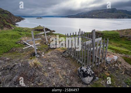 Le village de Sarfannguit près de Sisimiut au Groenland présente des tombes abandonnées surplombant des eaux tranquilles et des collines lointaines sous un ciel gris. Banque D'Images