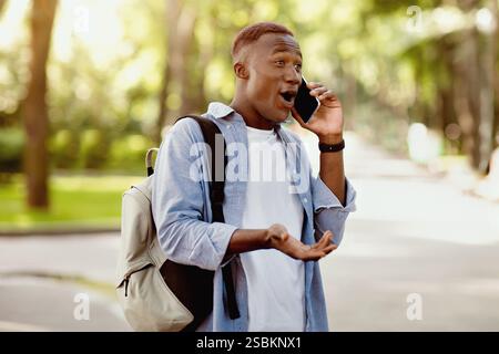 Surprise homme noir ayant la conversation sur téléphone mobile au parc Banque D'Images