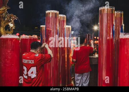 Balikpapan, Indonésie - 28 janvier 2025. Le père et le fils prient pour accueillir le nouvel an chinois, flanqué de grandes bougies rouges. Banque D'Images