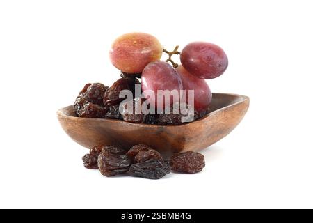 Un bol en bois rempli de raisins secs sombres et dosés se trouve à côté d'un bouquet de raisins rouges, suggérant le processus de séchage des raisins en raisins secs. Banque D'Images