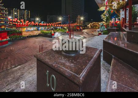 Balikpapan, Indonésie - 28 janvier 2025. Une cour de temple chinois avec encens brûlants et lanternes rouges, sur fond d'un contemporain Banque D'Images