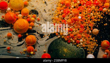 Liquide pétillant. Éclatement de la bulle de peinture. Particules rondes scintillantes qui se répandent dans l'eau noire. Fond abstrait de flou éclatant de pigment rouge orange. Banque D'Images