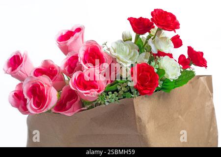 Un superbe bouquet de roses artificielles roses, rouges et blanches au feuillage luxuriant dans un sac en papier sur fond blanc, parfait pour la décoration, cadeau Banque D'Images