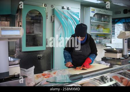 Busseto, Parme, Italie - 31 janvier 2025 poissonnier portant des gants et des vêtements d'hiver tranchant un filet de saumon avec un couteau sur une planche à découper en elle Banque D'Images