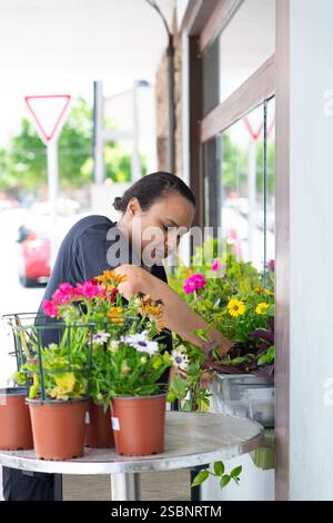 Fleuriste arrangeant des fleurs colorées dans des pots sur une table à l'extérieur d'un magasin de fleurs Banque D'Images