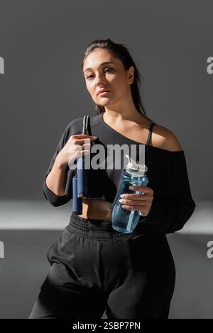 Femme confiante pose avec des équipements de fitness, démontrant force et vitalité dans un studio bien éclairé. Banque D'Images