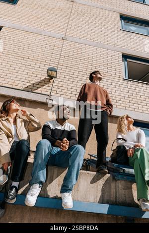 Vue en angle bas des étudiants masculins et féminins posant près du mur de briques sur le campus Banque D'Images