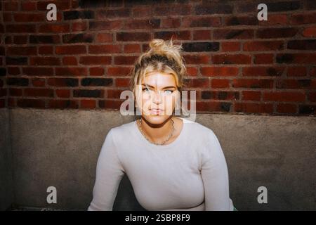 Portrait de belle femme blonde assise contre un mur de briques Banque D'Images