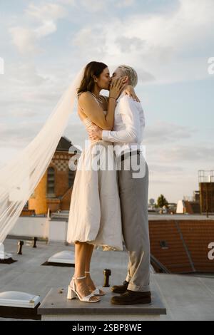 Couple romantique nouvellement marié s'embrassant tout en se tenant debout sur le toit Banque D'Images