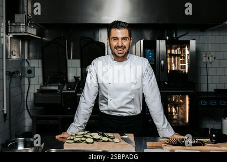 Portrait de jeune homme heureux chef debout près du comptoir avec des légumes hachés dans la cuisine au restaurant Banque D'Images