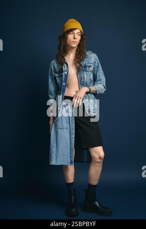 Un jeune homme élégant se dresse sur une toile de fond solide, mettant en valeur des choix de mode denim uniques. Banque D'Images