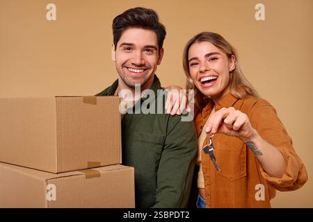 Un jeune couple joyeux et heureux célèbre leur nouvelle maison avec des boîtes mobiles et des clés dans leurs mains, mettant en valeur leur enthousiasme et happ Banque D'Images