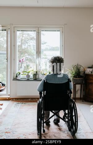 Vue arrière d'une femme âgée assise en fauteuil roulant en maison de retraite Banque D'Images