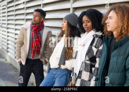 Quatre étudiants universitaires divers portant des vêtements d'hiver sont appuyés contre un mur extérieur d'un bâtiment du campus Banque D'Images