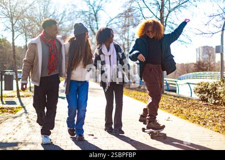 Quatre jeunes amis joyeux marchent et skateboard par une journée ensoleillée, profitant de leur temps ensemble à l'extérieur Banque D'Images