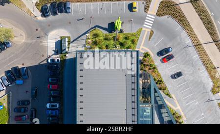 Vue aérienne d'un parking avec plusieurs voitures stationnées autour d'un bâtiment moderne. L'image montre une personne nettoyant les fenêtres d'une grue, avec un petit Banque D'Images