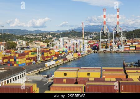 Vue en angle élevé de conteneurs d'expédition de boîtes métalliques rectangulaires empilés, de camions de transport et de manutentionnaire de conteneurs sur le quai dans le port de la Spezia, Italie, UE Banque D'Images
