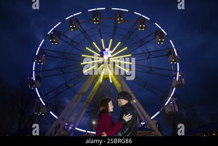 Couple regardant l'un à l'autre sous une grande roue brillamment éclairée contre un ciel sombre Banque D'Images