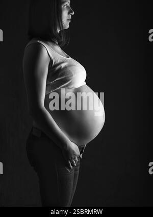 Femme enceinte, future mère sur fond noir, gros plan du ventre enceinte, activité pendant la grossesse, pousse monoshrome Banque D'Images