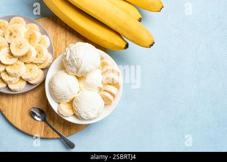 Cuillères à crème glacée et tranches de banane dans un bol sur fond bleu, vue de dessus, espace de copie. Crème glacée banane végétalienne crue saine (nicecream), bio maison Banque D'Images