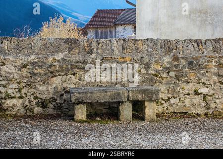 Un banc en pierre devant un mur de pierre traditionnel dans le village historique d'Andreis. Province de Pordenone, Frioul-Vénétie Julienne, nord-est de l'Italie. Banque D'Images