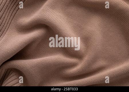 Une vue rapprochée du tissu tricoté brun doux affiché en douceur sur une surface plane, soulignant sa texture et ses plis doux. La lumière naturelle renforce la chaleur et l'attrait du matériau. Banque D'Images