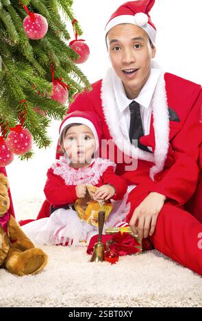 Famille heureuse dans la veille de Noël à la maison assis près de sapin décoré sur fond blanc, Porter du rouge Santa hats Banque D'Images