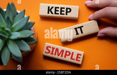 Symbole garder simple. Les mots conceptuels gardent la simplicité sur les blocs de bois. Main d'homme d'affaires. Beau fond orange avec plante succulente. Entreprise et Banque D'Images