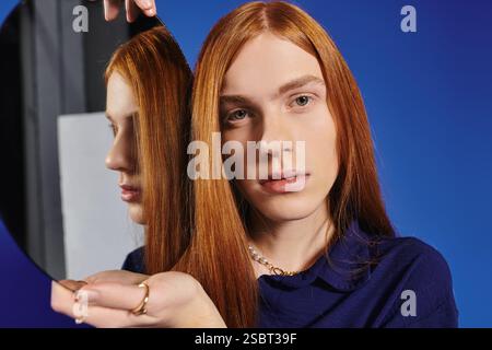 Un homme jeune et à la mode se tient confiant avec de longs cheveux roux, soulignant son style unique. Banque D'Images