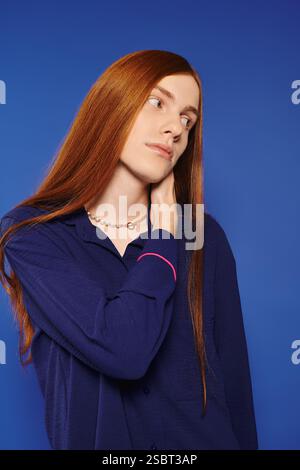 Un jeune homme à la mode avec de longs cheveux roux se tient confiant, mettant en valeur son style moderne. Banque D'Images