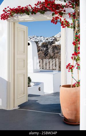 Vue sur les falaises de Santorin et le soleil à travers une arche avec une porte ouverte et bougainvilliers en fleurs, Cyclades, Grèce Banque D'Images
